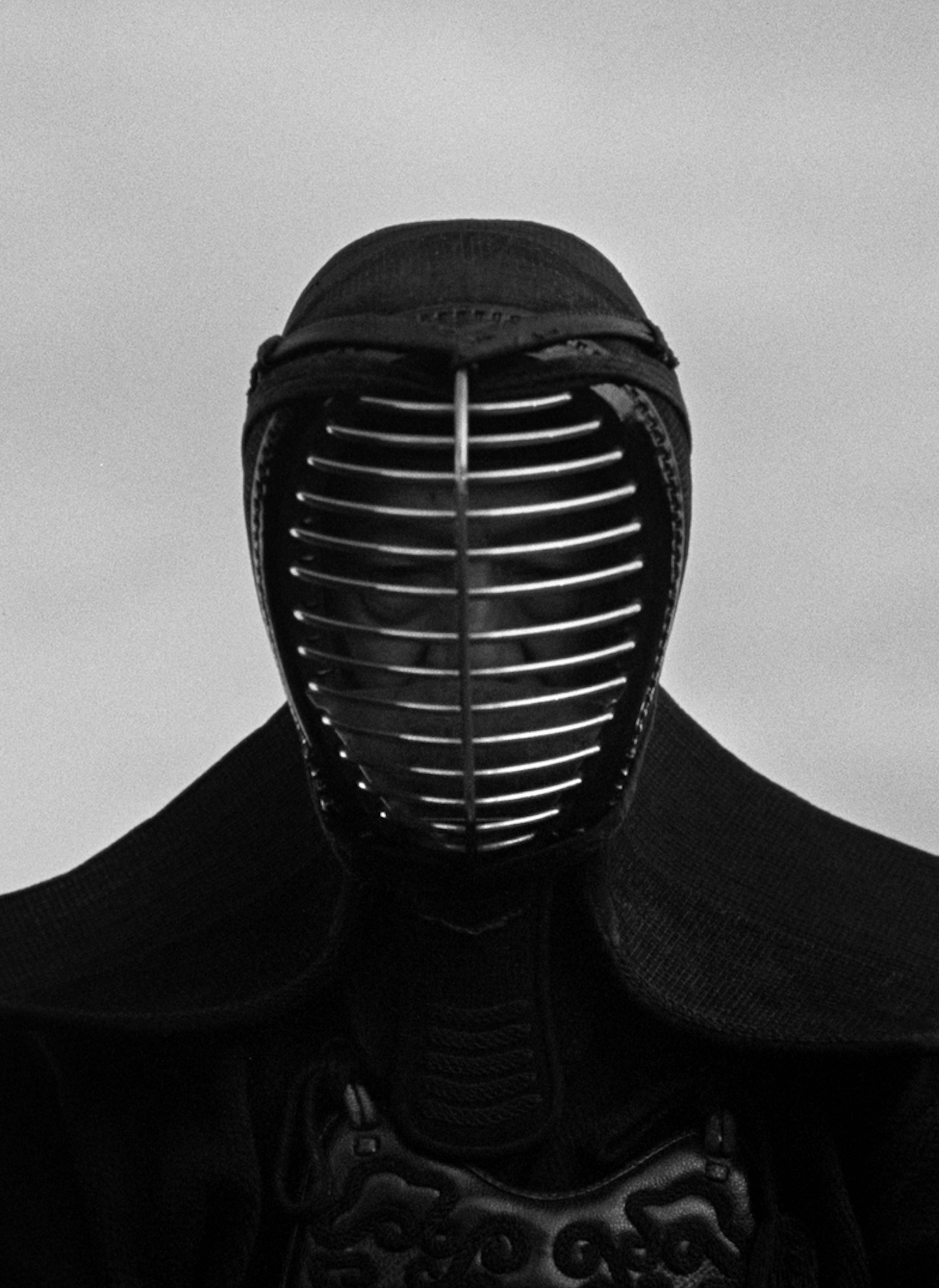 Close-up of a person wearing traditional black kendo armor with a protective metal face grill.