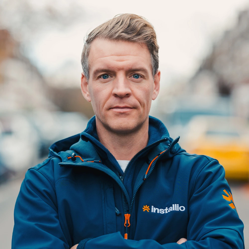 Portrait of a confident man wearing a blue Installio jacket with arms crossed standing outdoors.