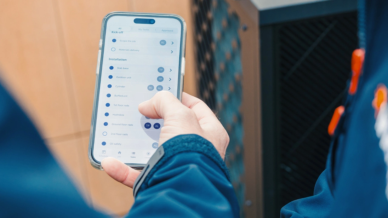 Person holding a smartphone displaying a task management app with a checklist for job kickoff and installation tasks.