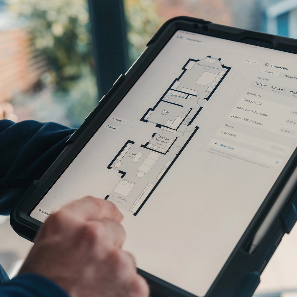 Person holding a tablet displaying a detailed floor plan with labeled rooms and dimensions.
