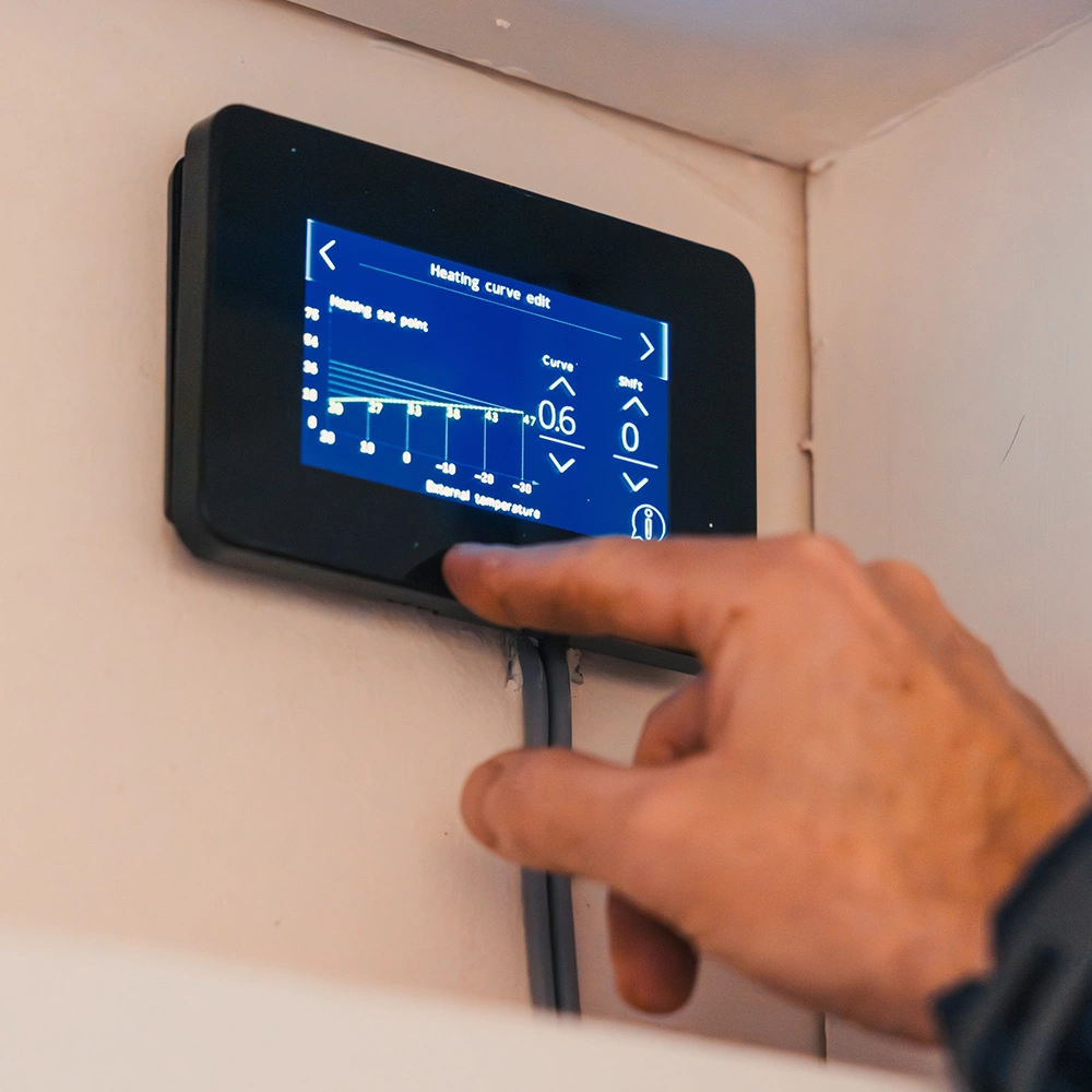 Hand adjusting settings on a digital thermostat displaying a heating curve edit screen mounted on a wall.