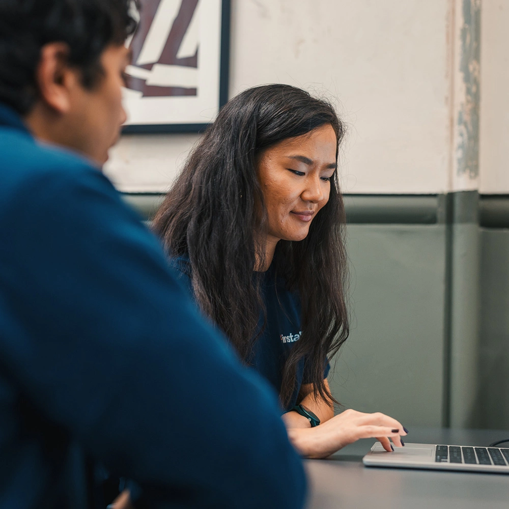 Woman with long hair focused on working on a laptop, while a man sits beside her in a casual office setting.
