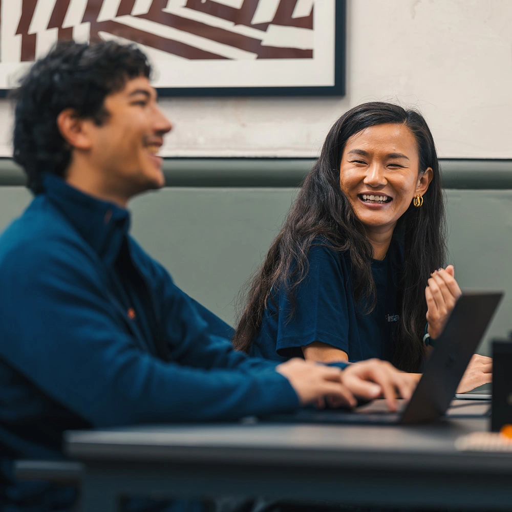 Two people smiling and working together on laptops in an office setting.