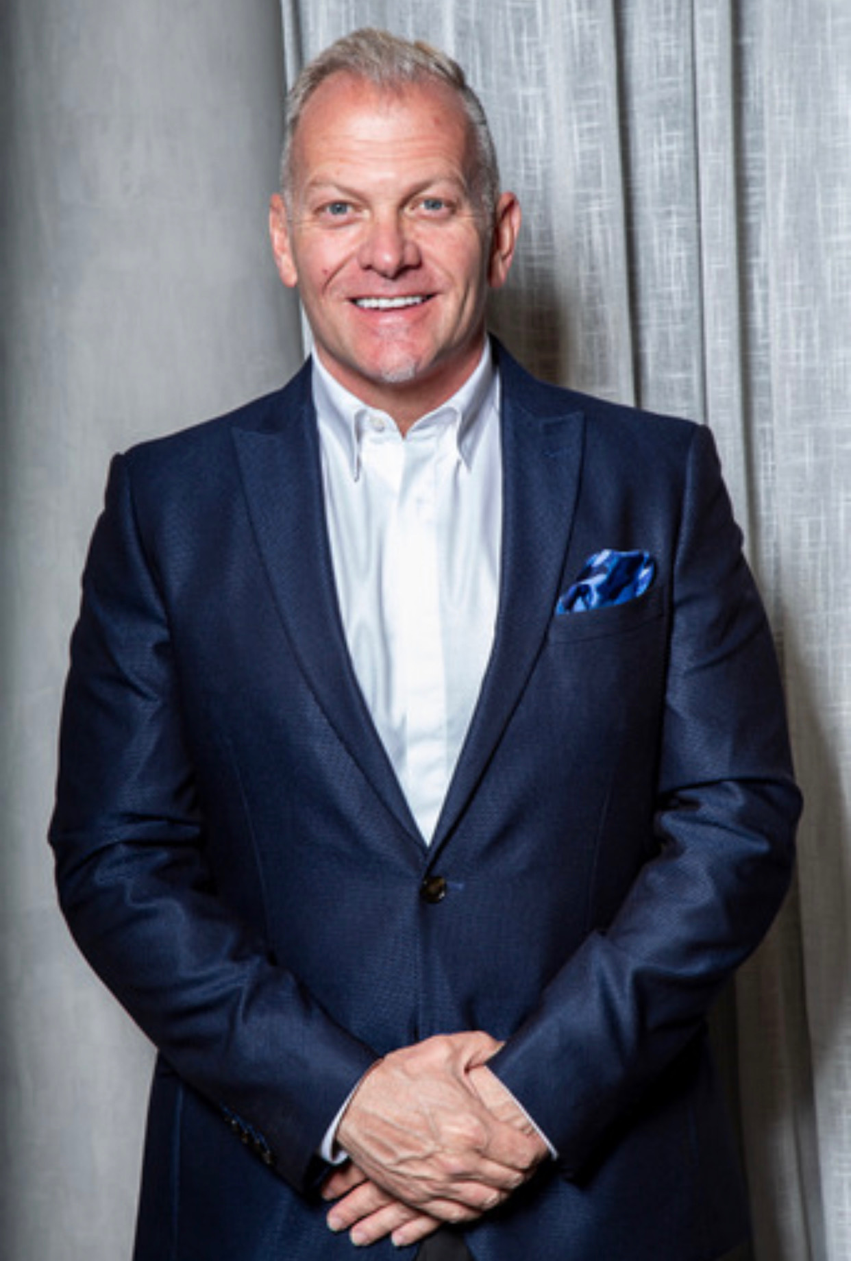 A photo f Kevin Milfeld - Board President of RISE Hybrid Academy in a blue suit and white shirt.