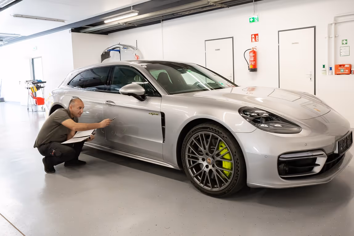 Man inspecting and pointing at a silver Porsche e-hybrid car in a bright garage.