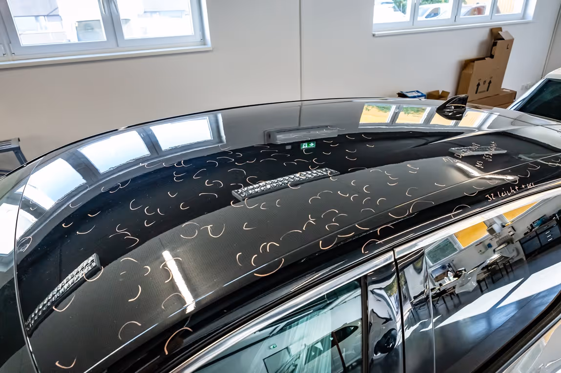 Top view of a glossy black car roof with white marker circles indicating dents inside a workshop.
