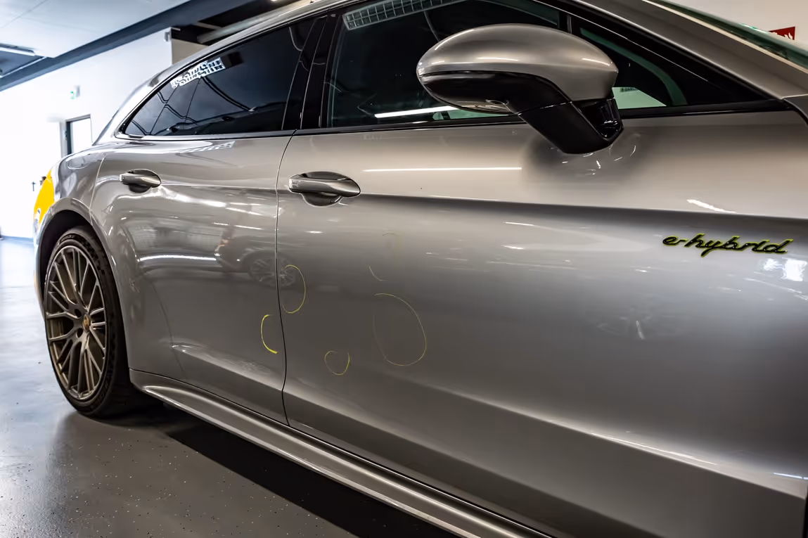 Silver car door with e-hybrid badge and several yellow circled dents ready for repair.