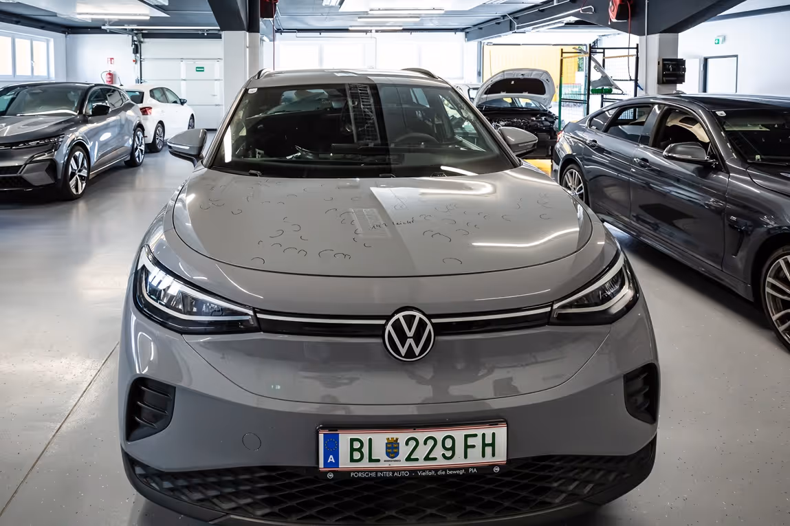 Front view of a gray Volkswagen electric car parked inside a showroom with other cars visible in the background.