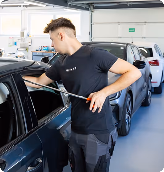 Man using a tool to unlock or open a car door inside a garage.