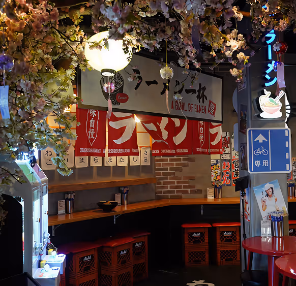 Cozy Japanese ramen restaurant interior with red stools, hanging cherry blossom decorations, and illuminated ramen signs.