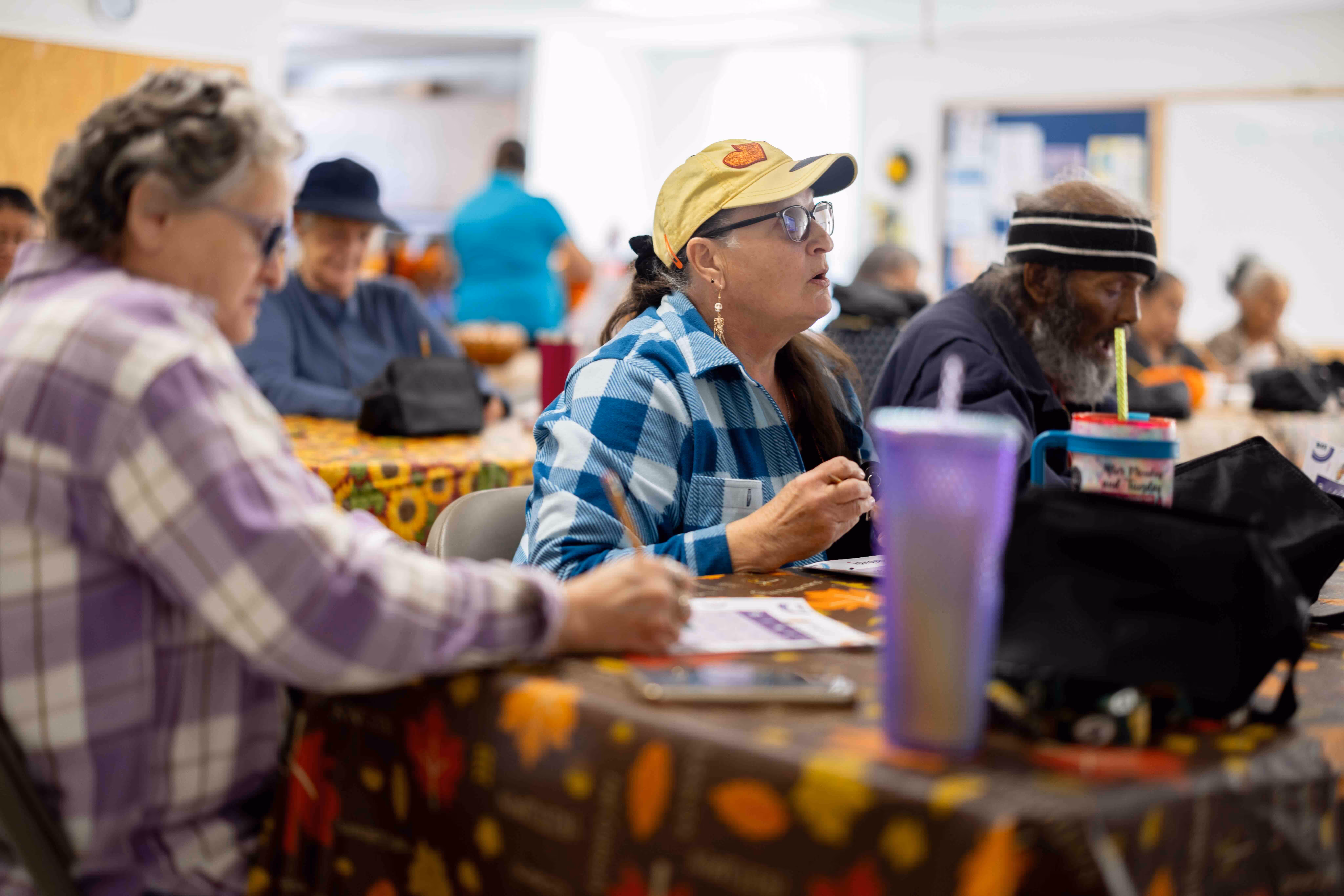 Older adults sitting at a table with autumn-themed tablecloth, engaging in activities with papers and pens.