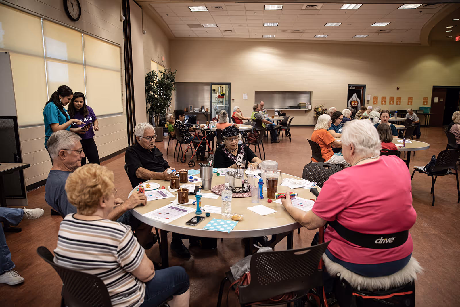 Group of elderly people sitting around tables playing bingo in a community center.