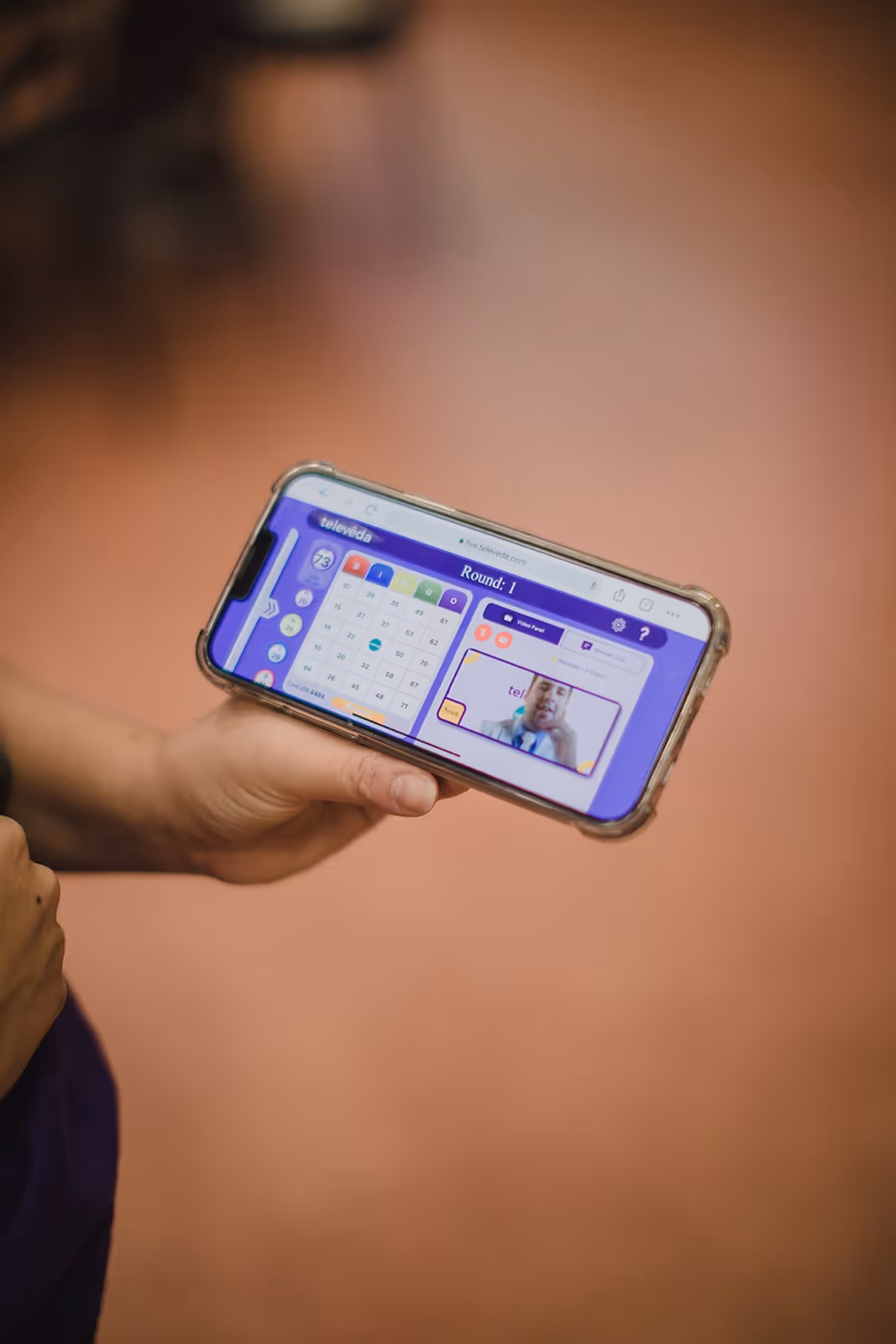 Hand holding a smartphone displaying a live online bingo game with a video call of a man in a suit.