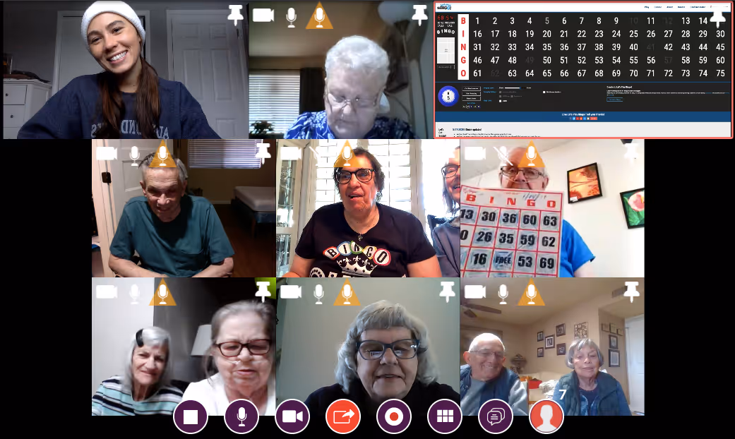 Video call screen showing nine participants playing Bingo, with one holding up a Bingo card and a Bingo game board visible.