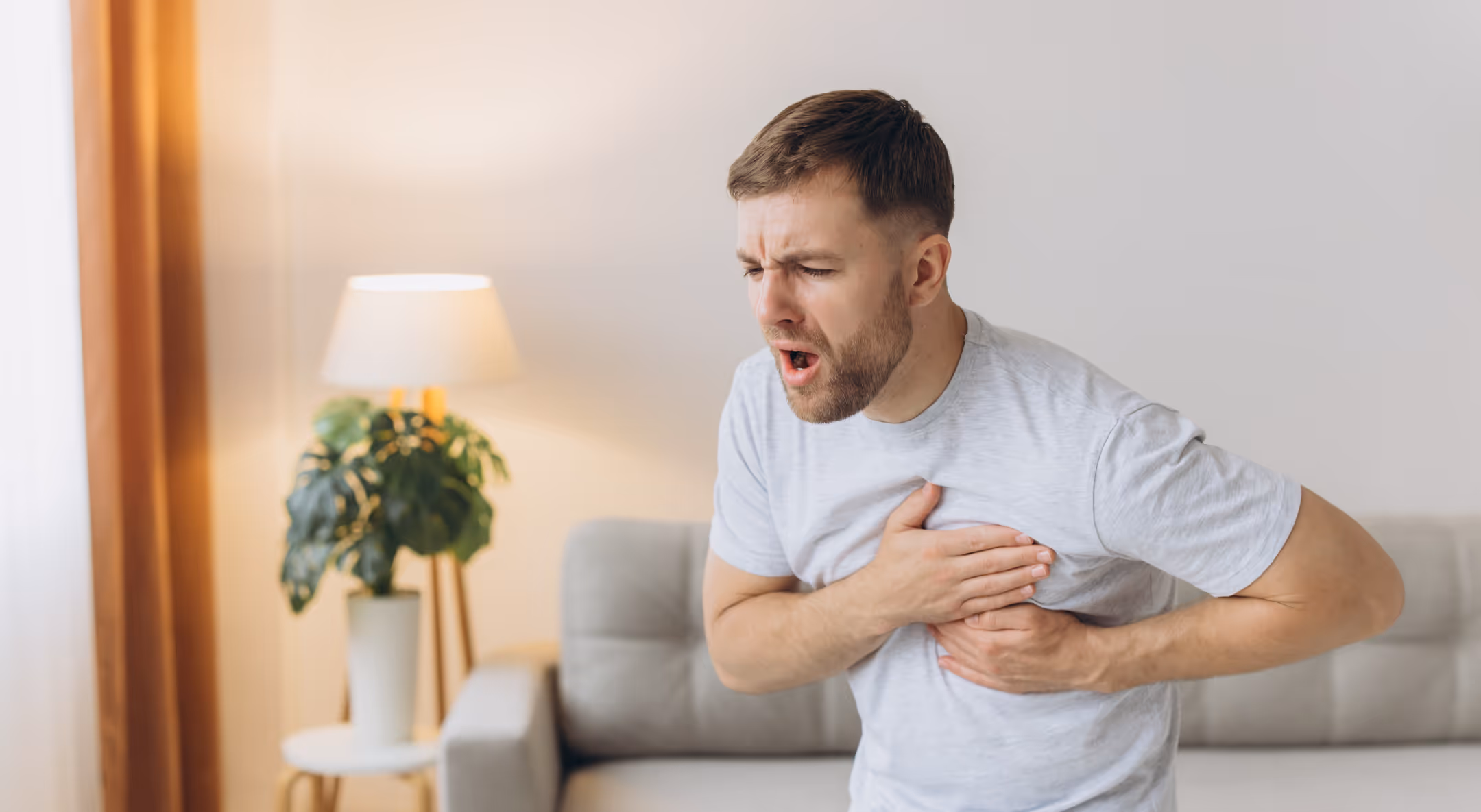 Man experiencing signs of a heart attack at home, holding his chest in distress.