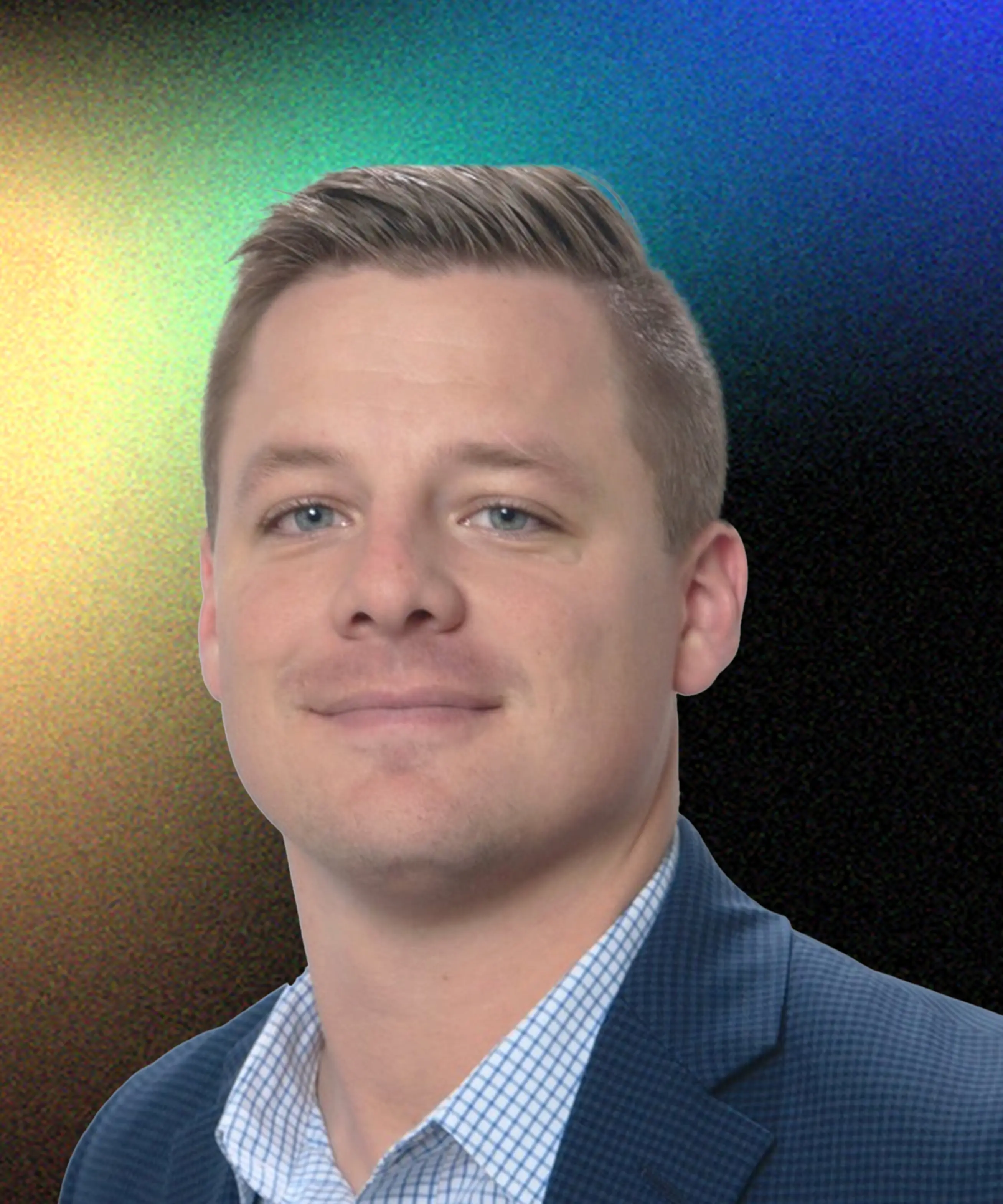 Portrait of a man with short blond hair wearing a blue checkered shirt and blue blazer, smiling slightly against a blurred colorful background.