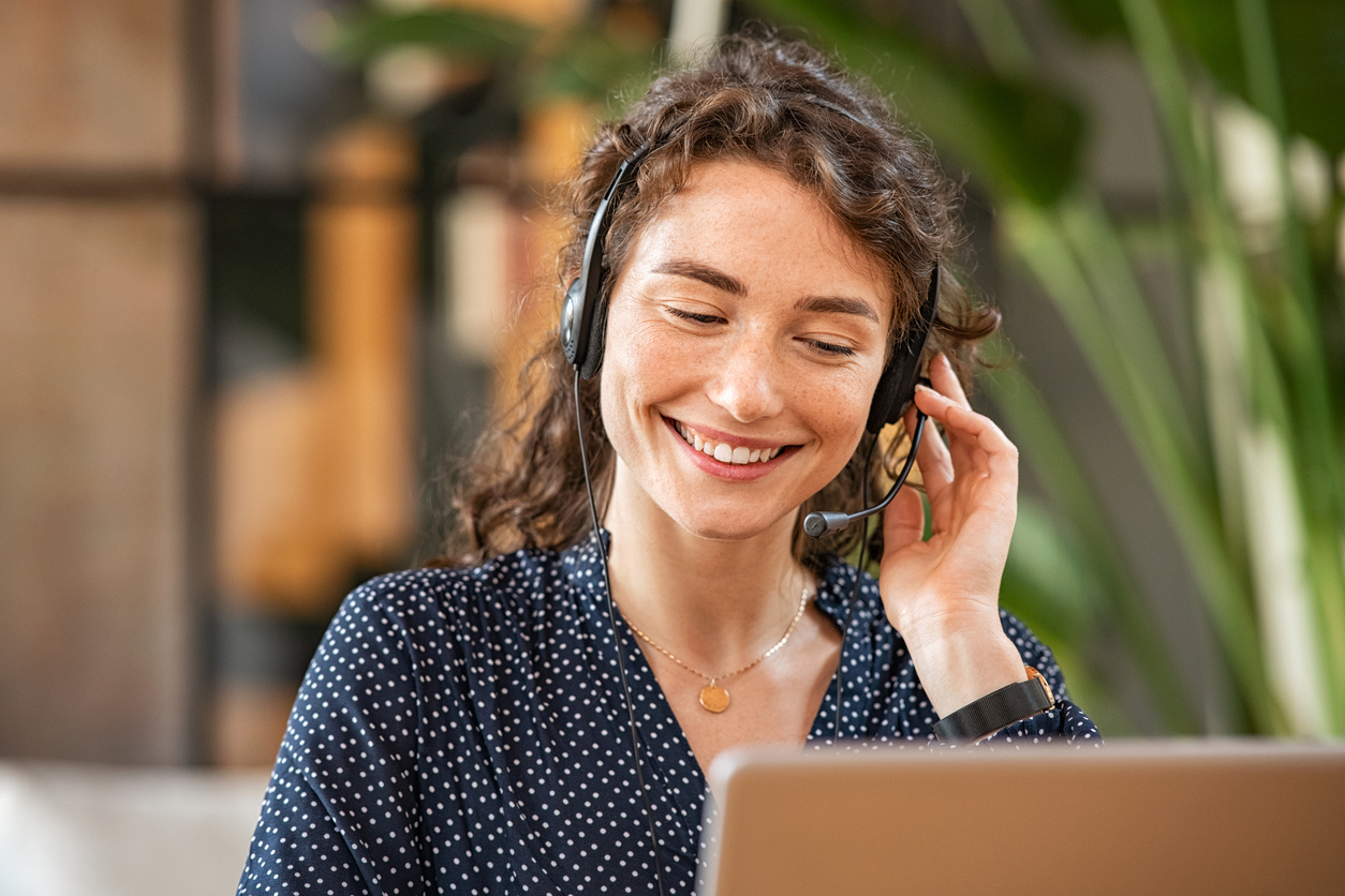Smiling woman with curly hair wearing a headset while looking at a laptop.