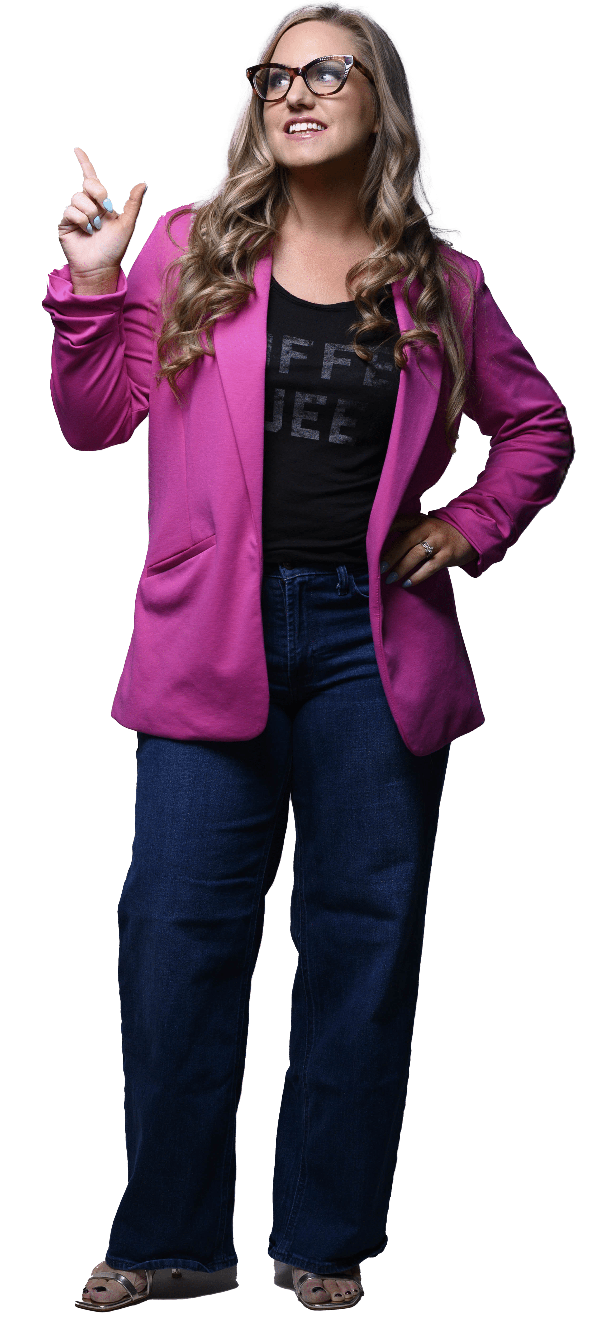 Smiling woman with long curly blonde hair wearing glasses, a bright pink blazer, dark jeans, and sandals, pointing upward with her left hand.