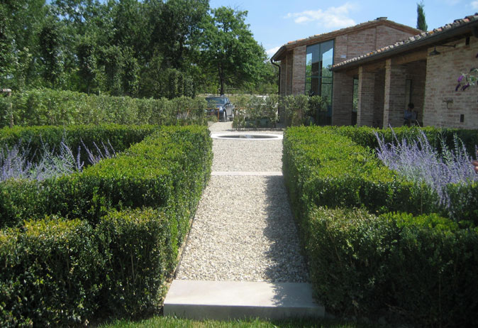 Formal Italian garden path with gravel, stone slabs, and manicured boxwood hedges leading to a fountain and brick villa.