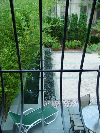 View from a balcony railing overlooking a contemporary water feature, bamboo wall, and a slatted patio lounge chair.