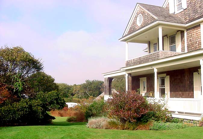 Shingle-style house porch overlooking a wide, gently sloped lawn and meadow plantings in coastal terrain.