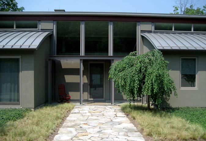 Flagstone walkway leading to the entrance of a modern home with curved metal roof and a weeping birch tree.