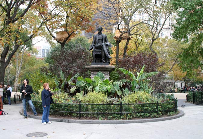 Statue of William Seward surrounded by lush, tropical-like plantings and a low black metal fence.