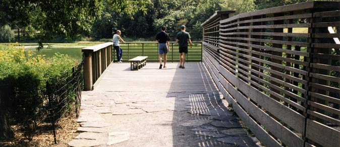 People walk on a wooden viewing platform featuring a slatted wooden privacy screen/railing.