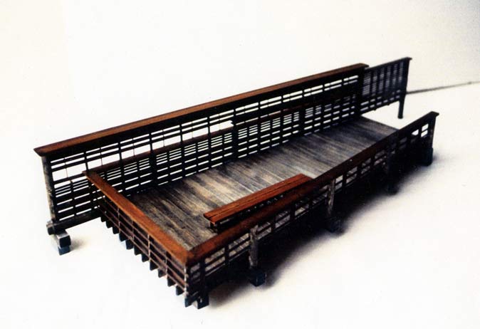 Model of the tiered wooden viewing deck/pier with high slatted railings and bench seating.