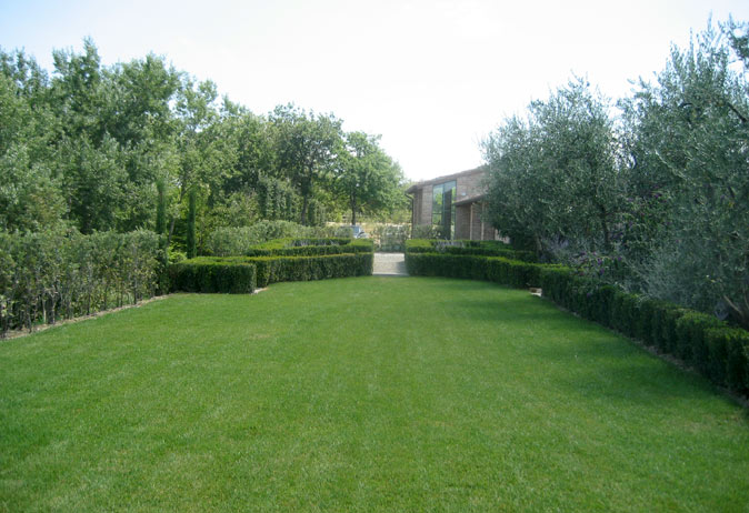 Wide, open lawn bordered by low, formal boxwood hedging, leading to the brick estate building in the distance.