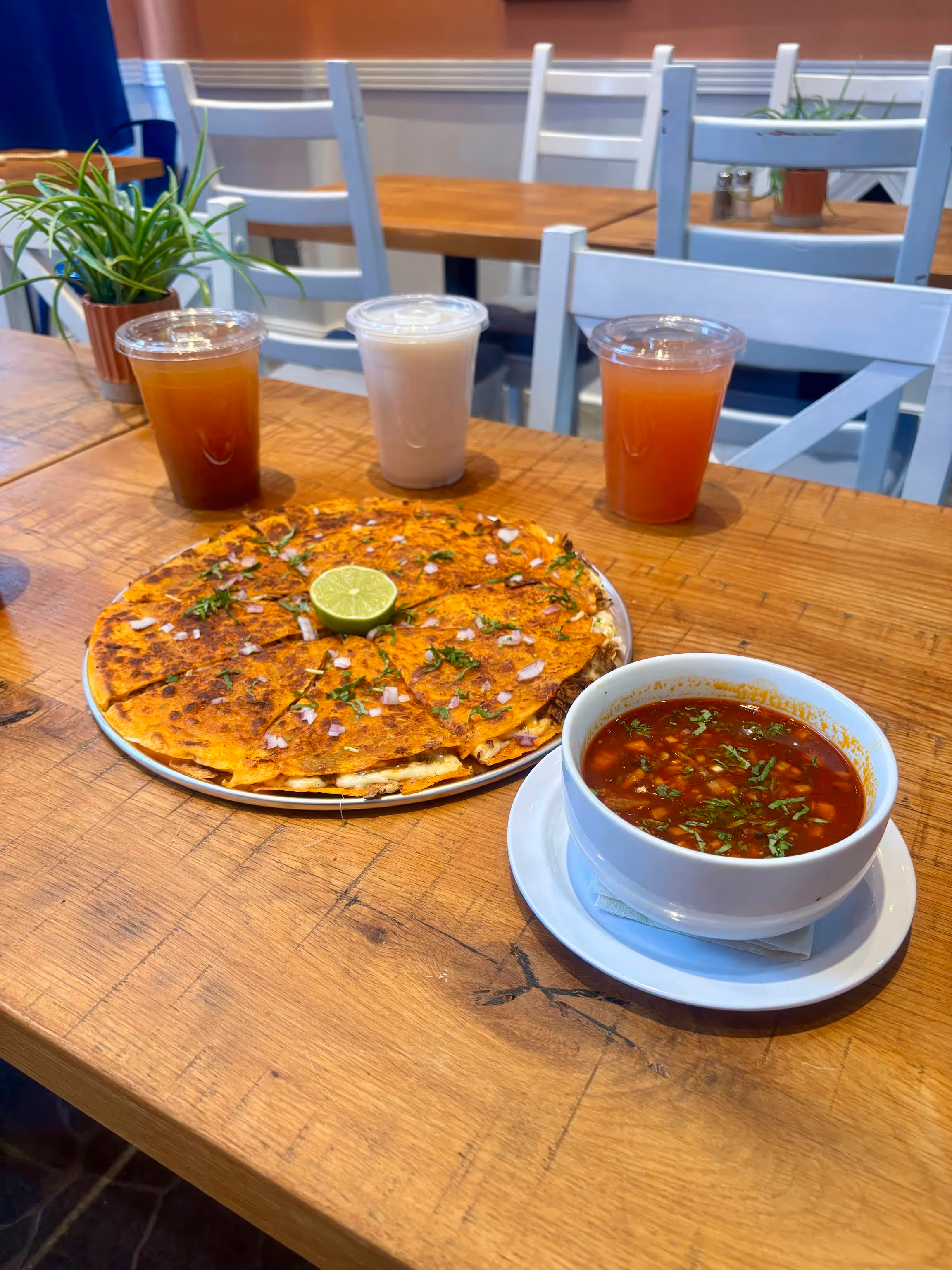 A table with a pizza, a bowl of soup, and two drinks on it.