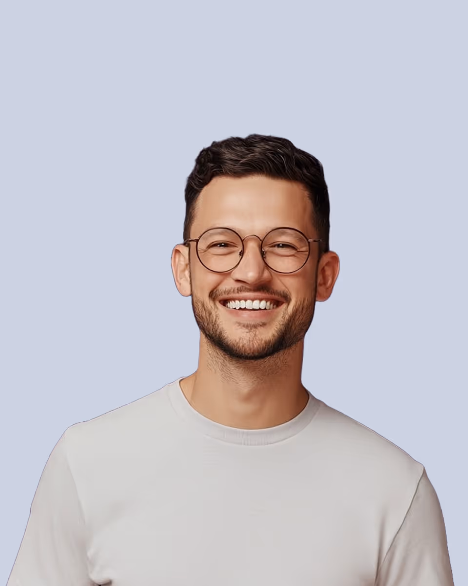 Smiling man with short dark hair, round glasses, and a light gray shirt against a plain light blue background.