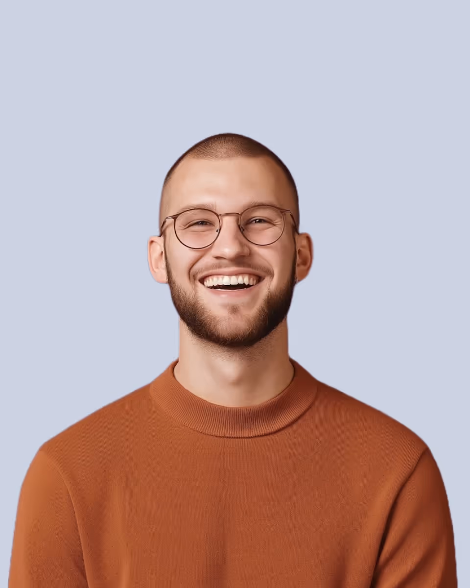 Smiling man with round glasses, short hair, and a beard wearing a rust-colored sweater against a light blue background.