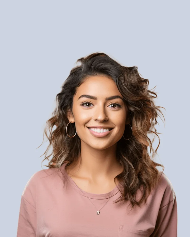 Smiling woman with wavy brown hair wearing hoop earrings and a pink shirt against a light gray background.