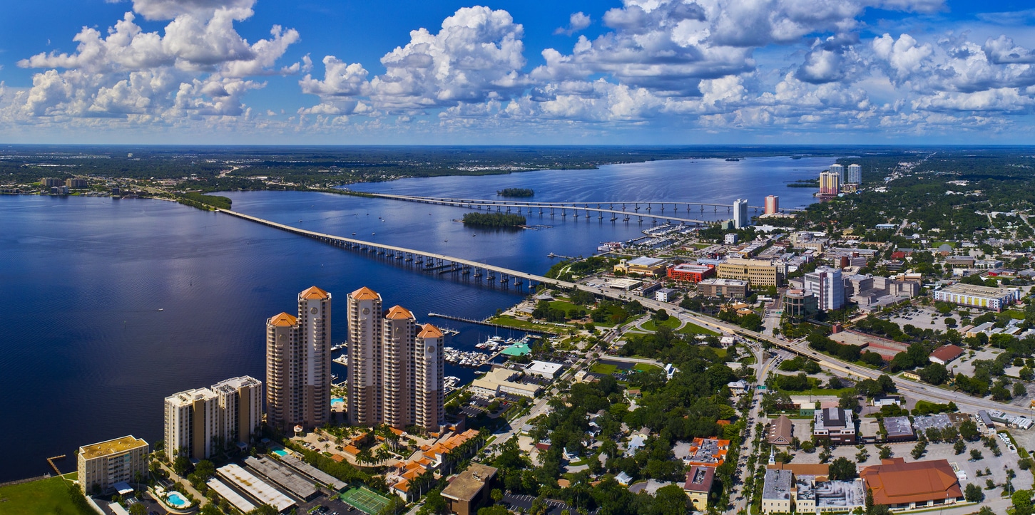 Aerial view of a coastal city with multiple bridges crossing a wide river under a partly cloudy blue sky.