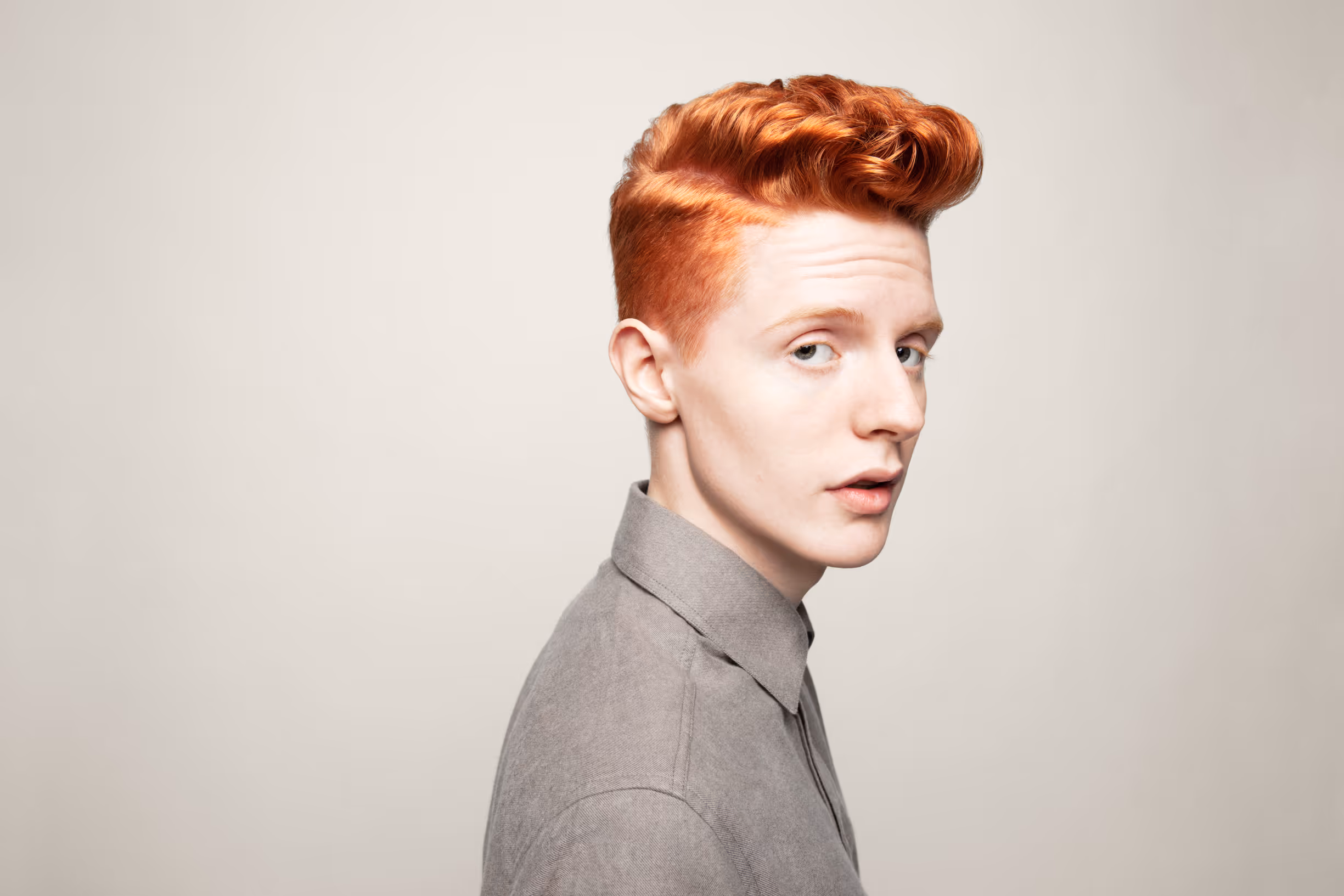 Ung mann med rødt hår og grå skjorte som ser over skulderen mot kameraet.