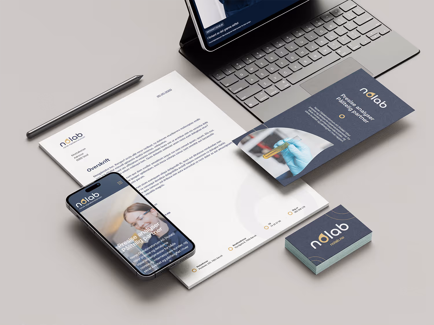 Bord med laptop, penn, papir, visittkort og mobil som viser profil for Norsk oljelaboratorium med blå og hvit design.