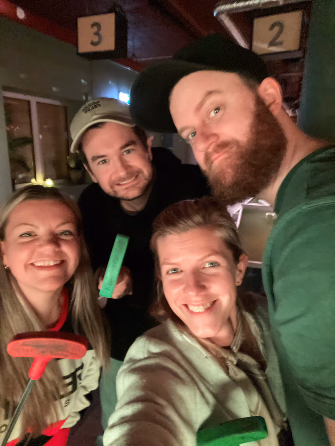 Fire glade venner som smiler og holder mini-golf køller innendørs.