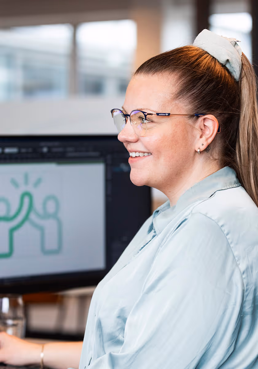 Kvinne med briller og hestehale smiler mens hun ser på en dataskjerm med et bilde av to figurer som gir high five.