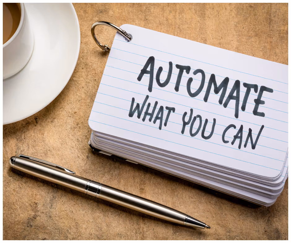 Stack of lined flashcards with metal ring and text 'AUTOMATE WHAT YOU CAN' written in bold black marker, alongside a silver pen and a cup of coffee on a wooden surface.