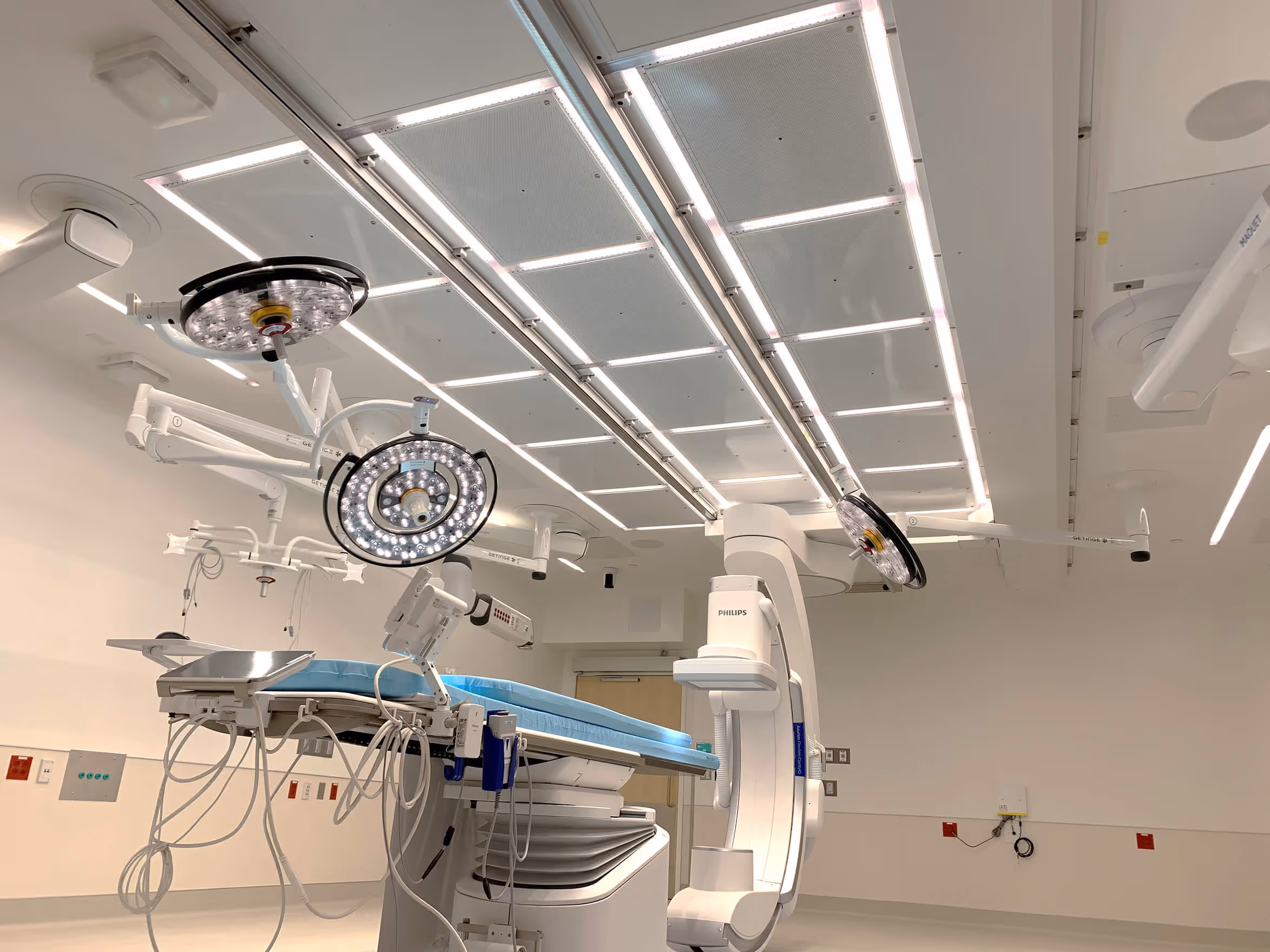Angiography suite with a large C-arm machine, surgical lights, and specialized ceiling lighting.