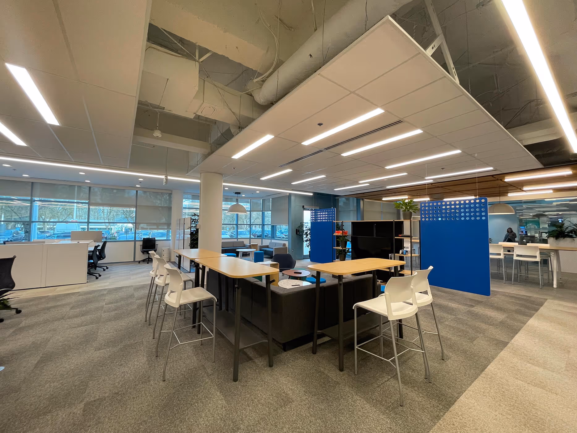 BCAA open office area with high collaboration tables and rectangular overhead lighting panel.