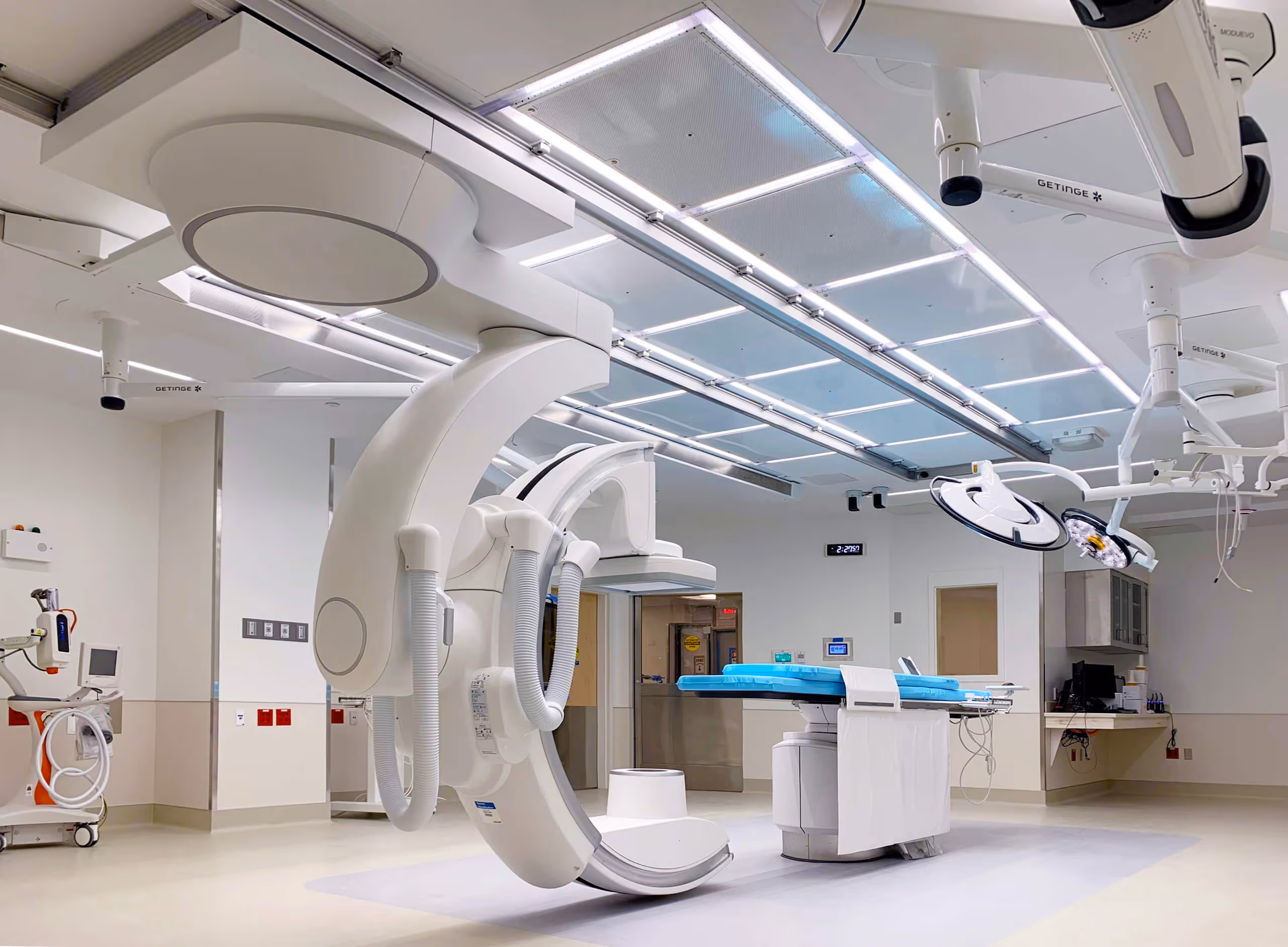 Modern angiography room with a large C-arm and multiple ceiling-mounted equipment arms.