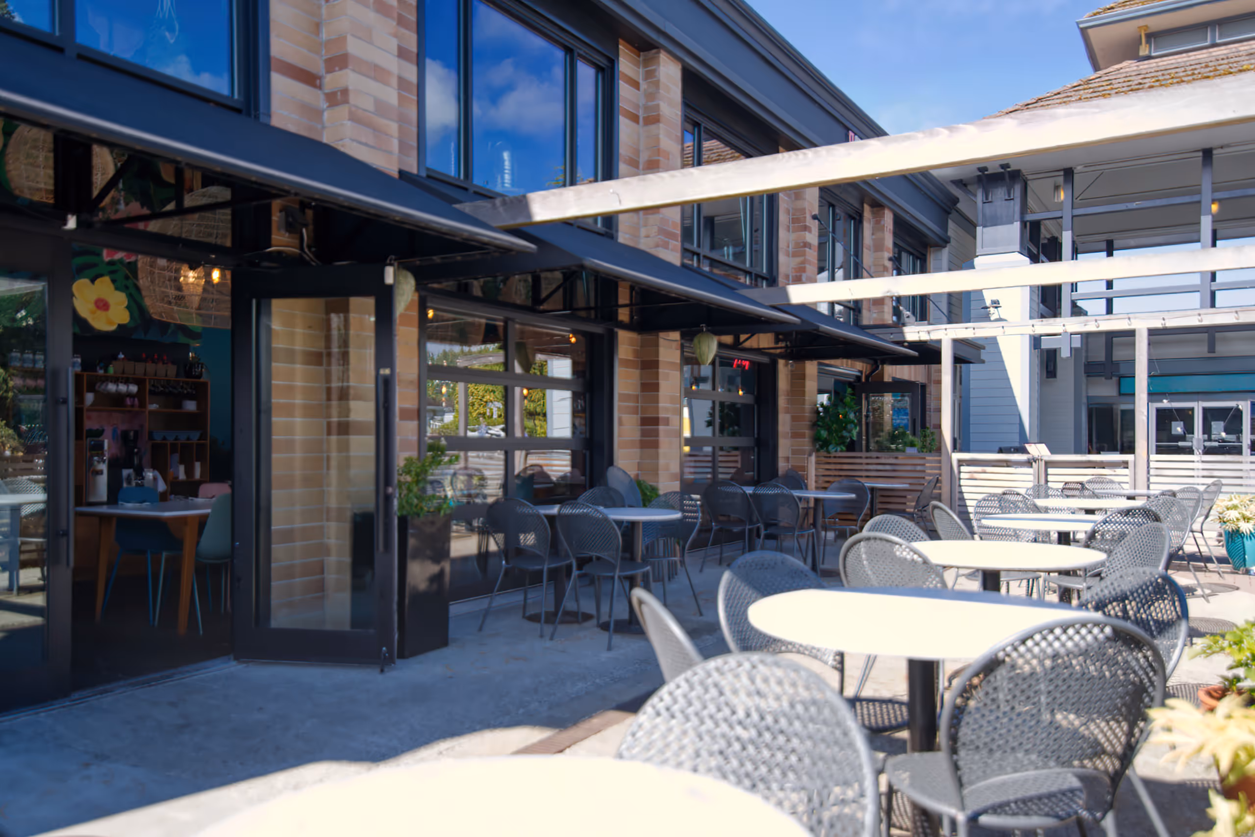 Sunlit outdoor patio with black mesh tables and open garage-style doors.