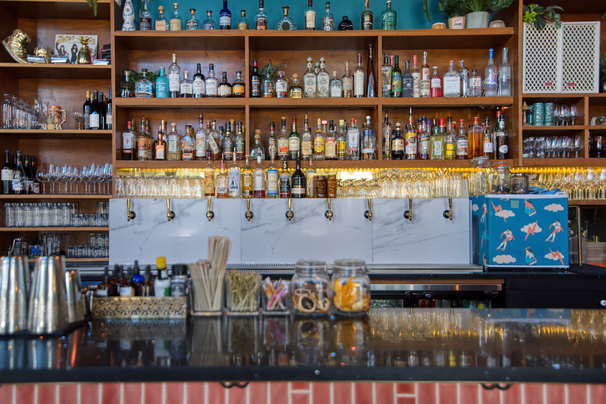 Illuminated bar shelving stocked with liquor bottles above gold beer taps.