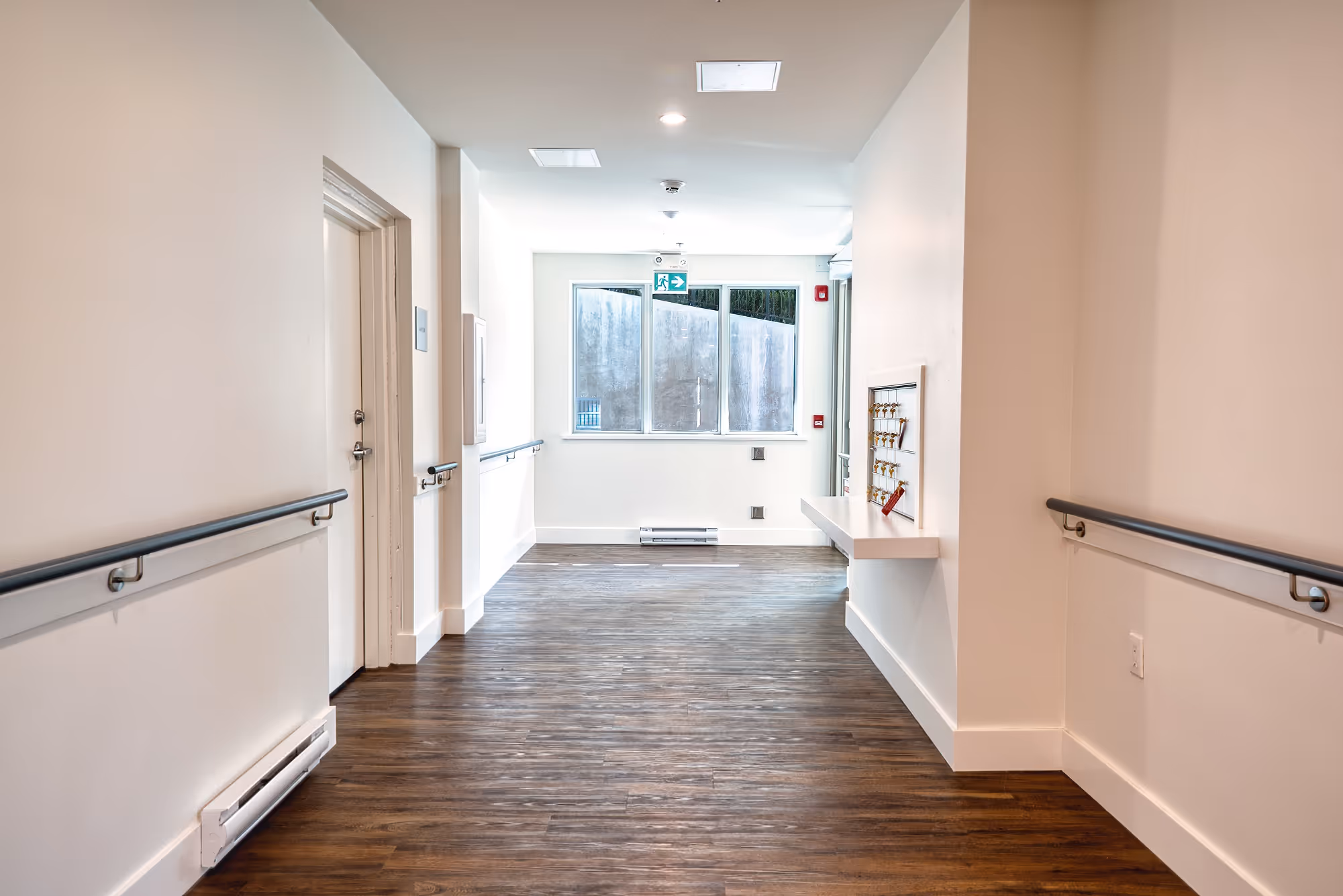 Interior corridor at Lily Lake Place Seniors Housing with handrails and emergency exit signage.