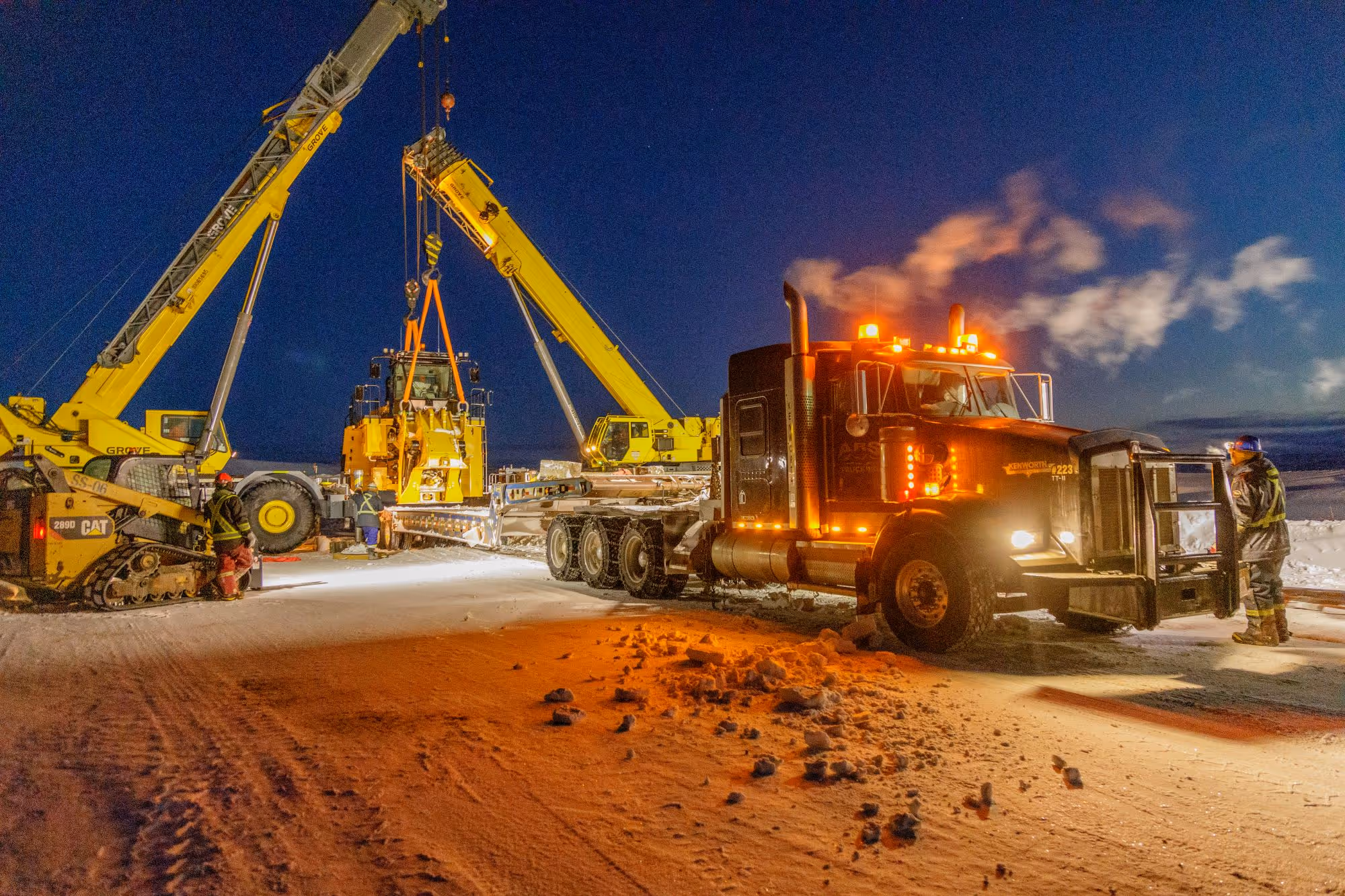 Night operation at Goose Lake project showing crane lift and transport truck on snowy site.
