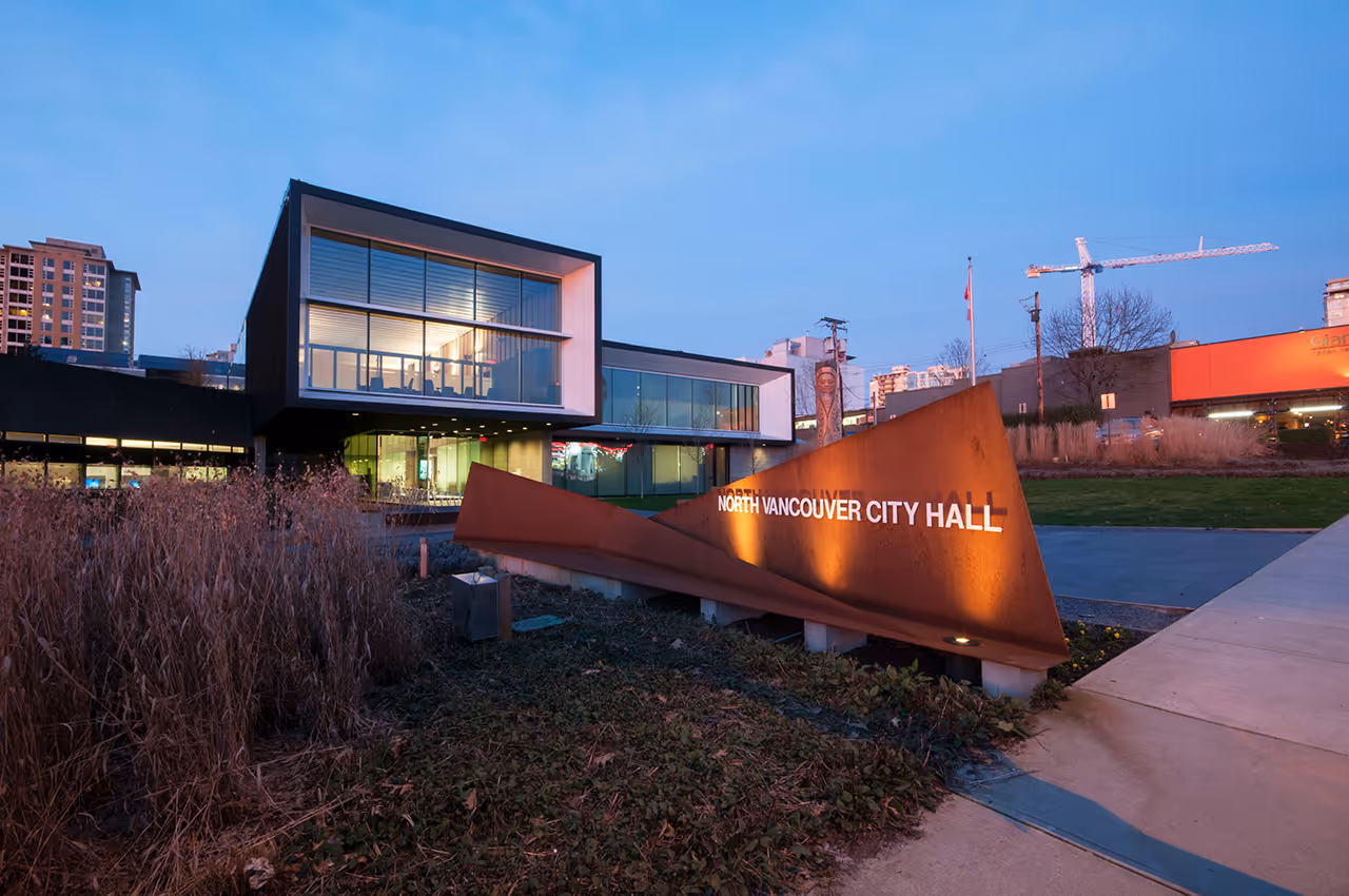 Exterior view of North Vancouver City Hall Redevelopment at dusk with illuminated windows and signage.