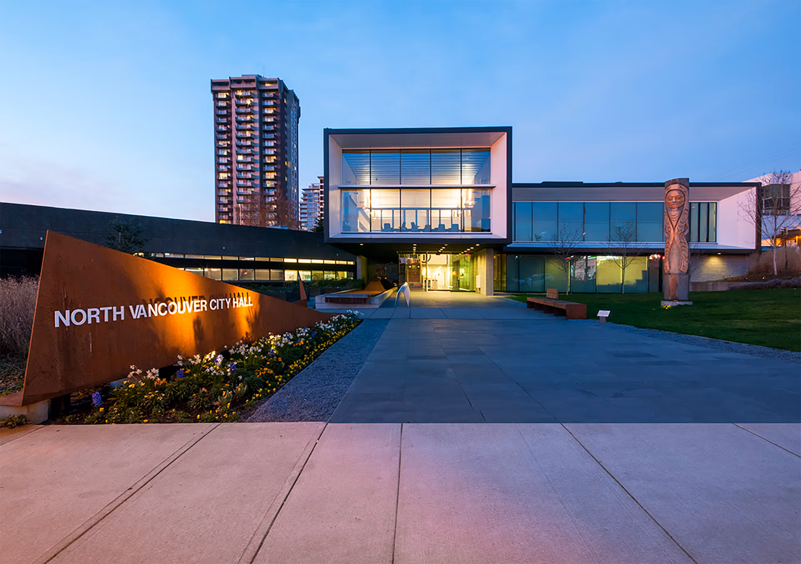 Exterior view of North Vancouver City Hall Redevelopment at dusk with illuminated windows and signage.