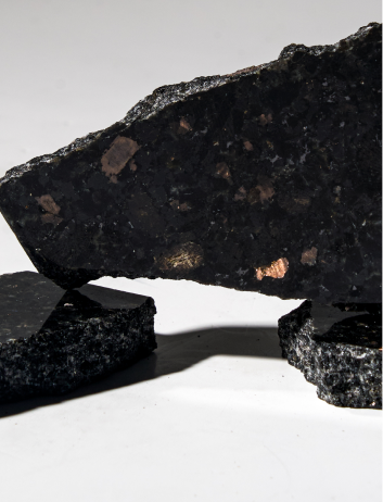 Close-up of dark, rough-textured stone pieces with reflective patches arranged on a white surface.